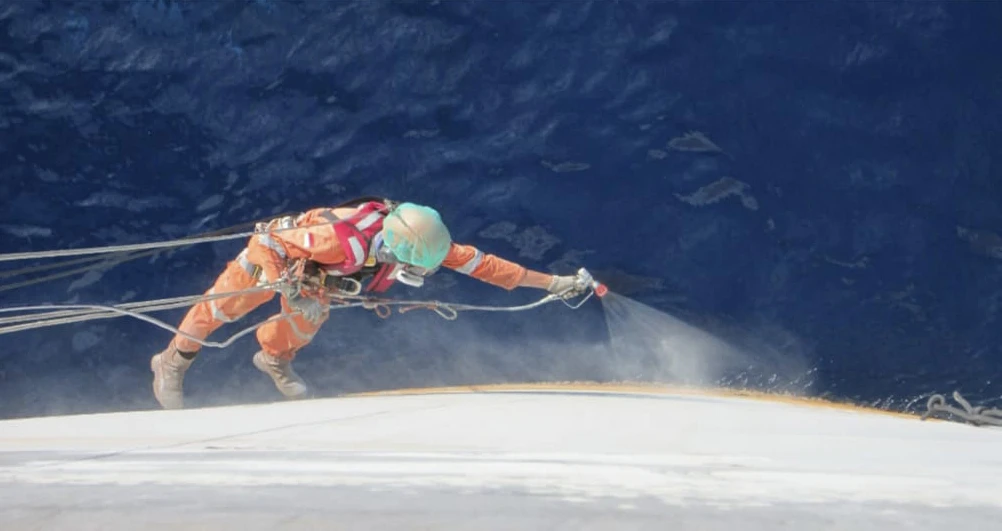 Rope-access technician hydroblasting a ship hull